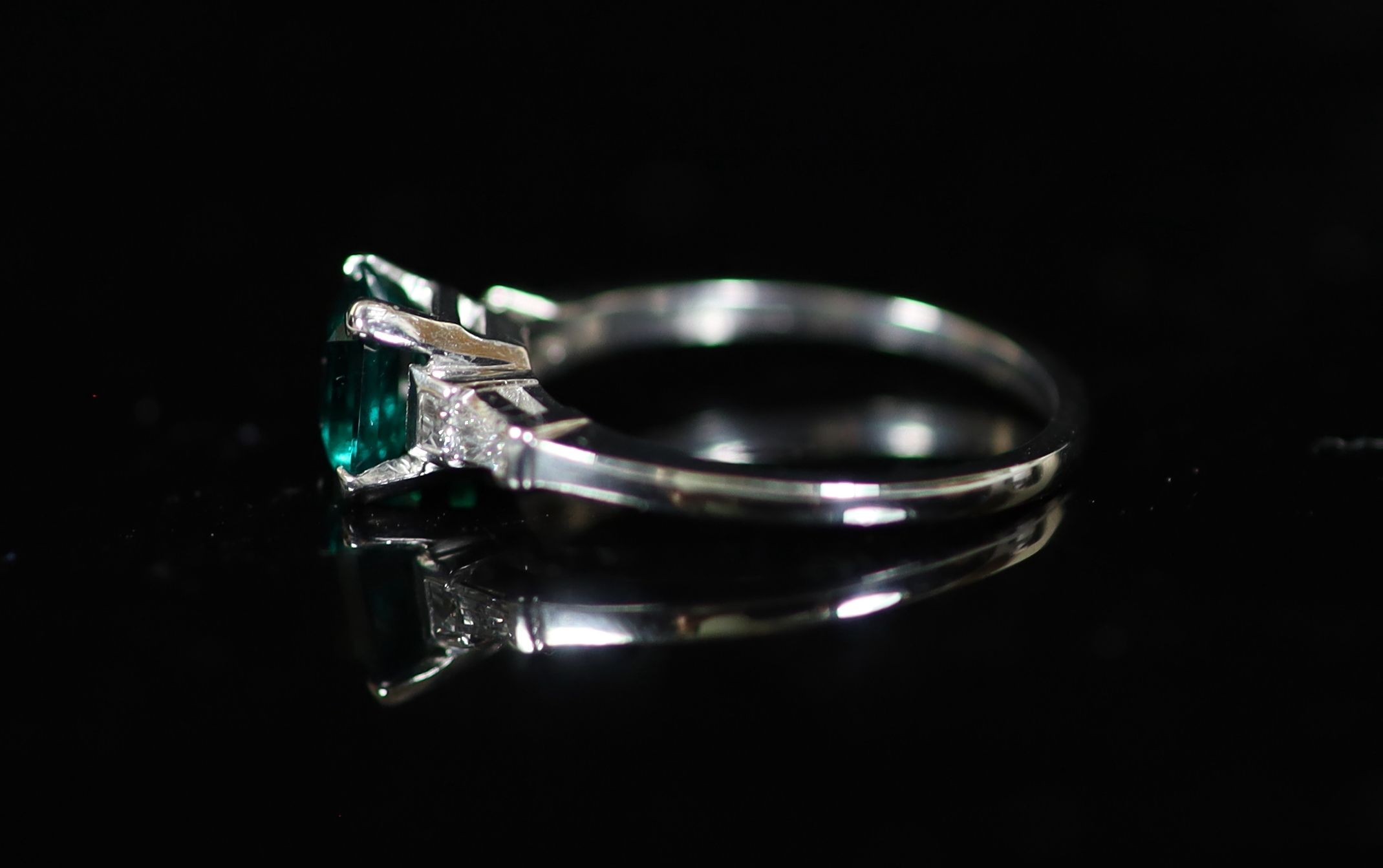 A platinum and single stone emerald ring with trapeze cut diamond set shoulders